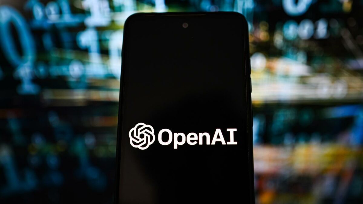 OpenAI logo is seen displayed on a smartphone with code in the background.